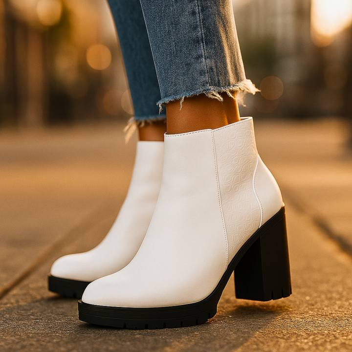 White ankle boots with black soles worn by a person on a blurred outdoor background